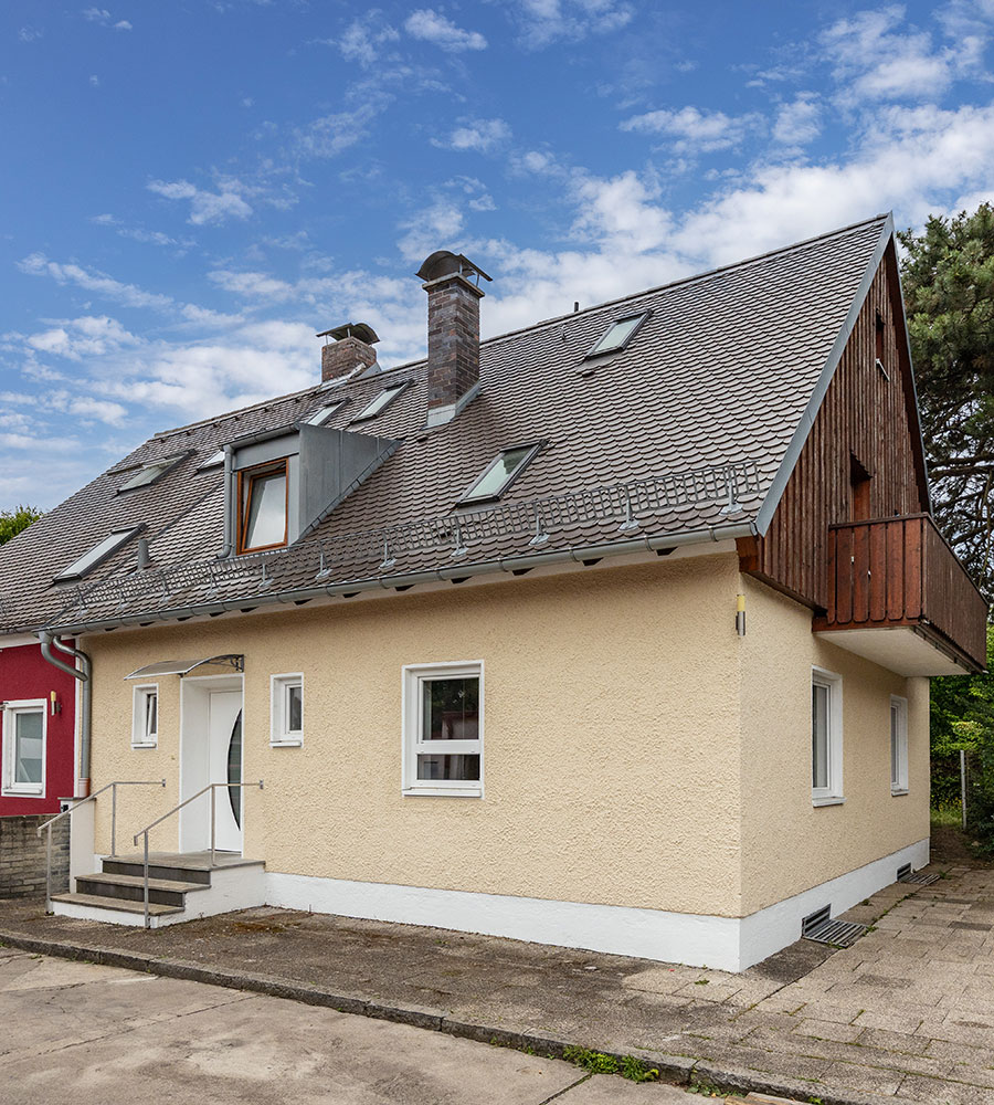 Gelbes Einfamilienhaus mit grauem Dach und Dachgauben unter blauem Himmel.