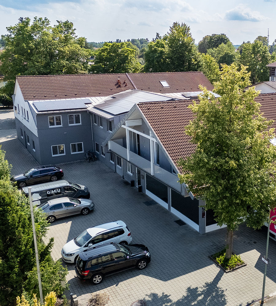 Luftaufnahme eines grauen Gebäudes mit roten Ziegeldächern und geparkten Autos.