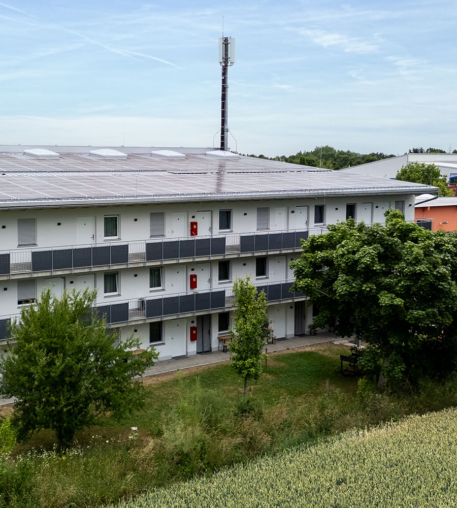 Ein modernes, weißes Gebäude mit Solaranlage und Bäumen im Vordergrund.