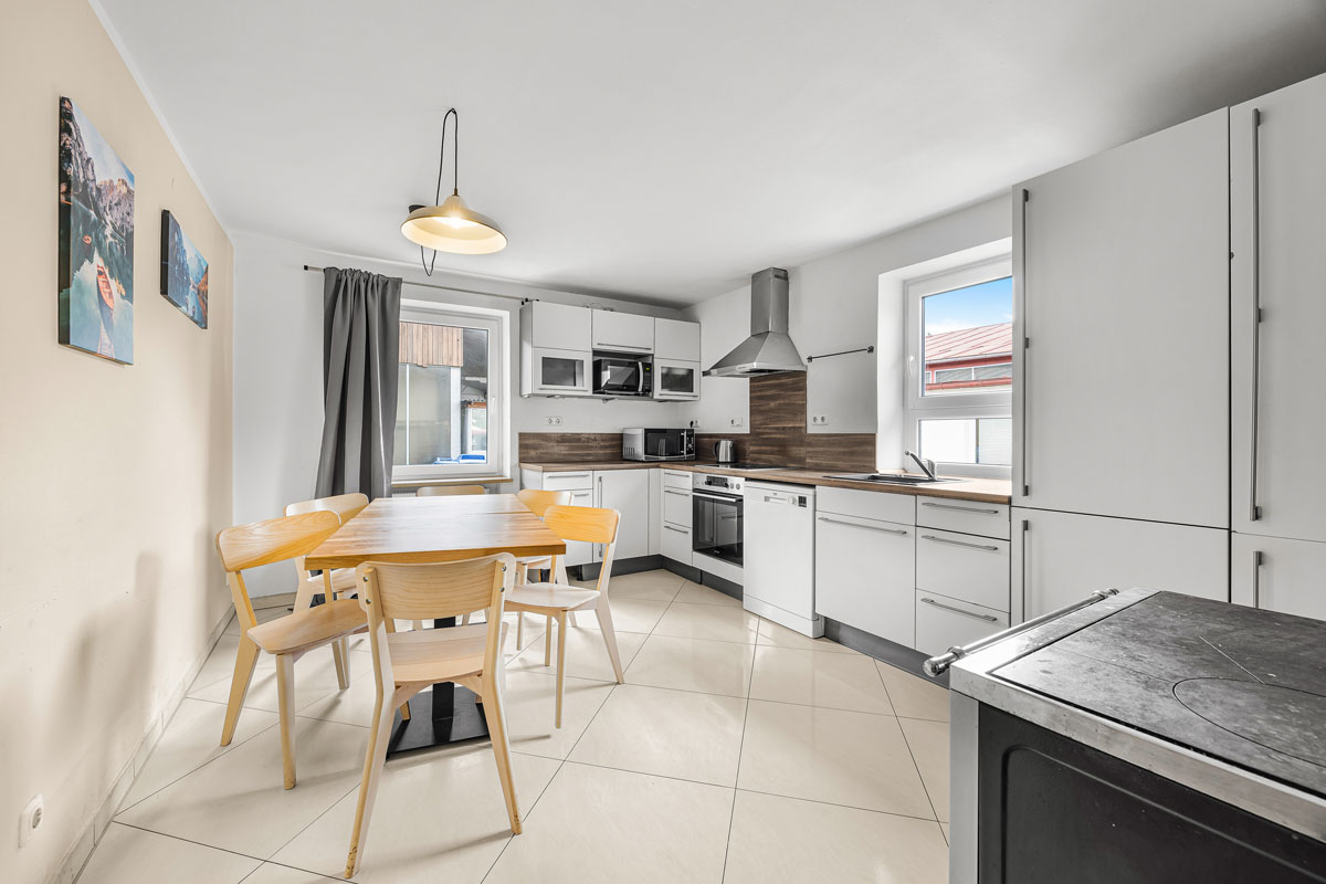 Eine moderne Küche mit Holztisch, hellen Stühlen und weißen Schränken.