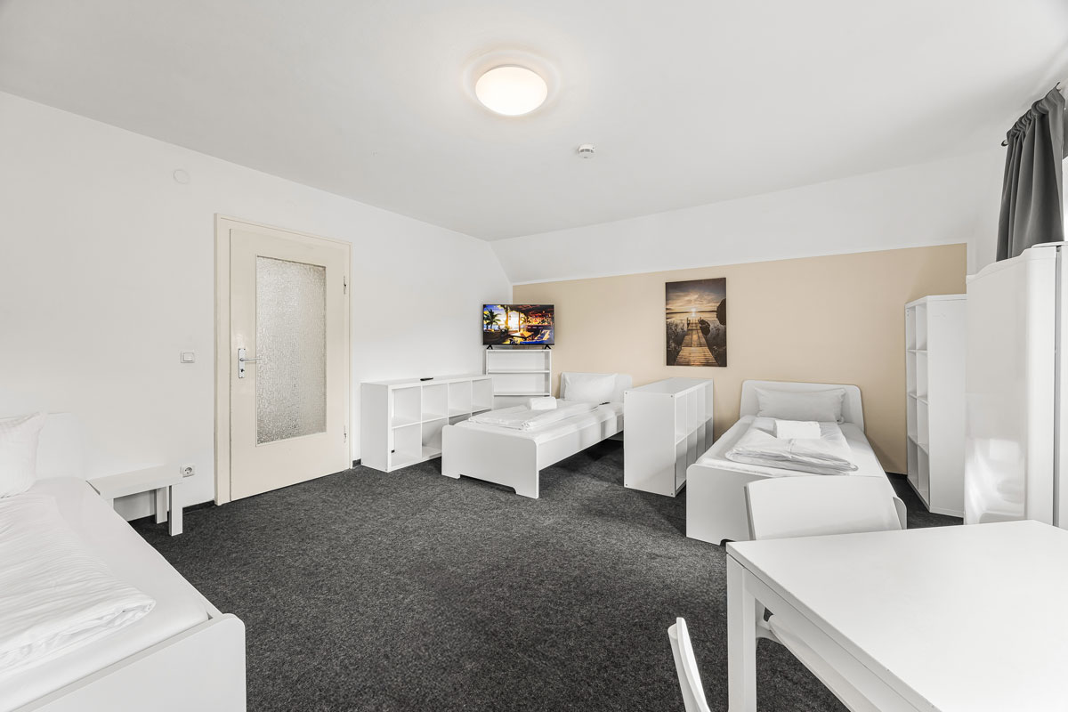 Helles Zimmer mit zwei Einzelbetten, Tisch und Sofa, alles in Weiß gehalten.