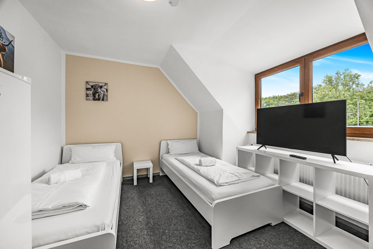 Ein helles Dachzimmer mit zwei weißen Einzelbetten und großem Fenster.