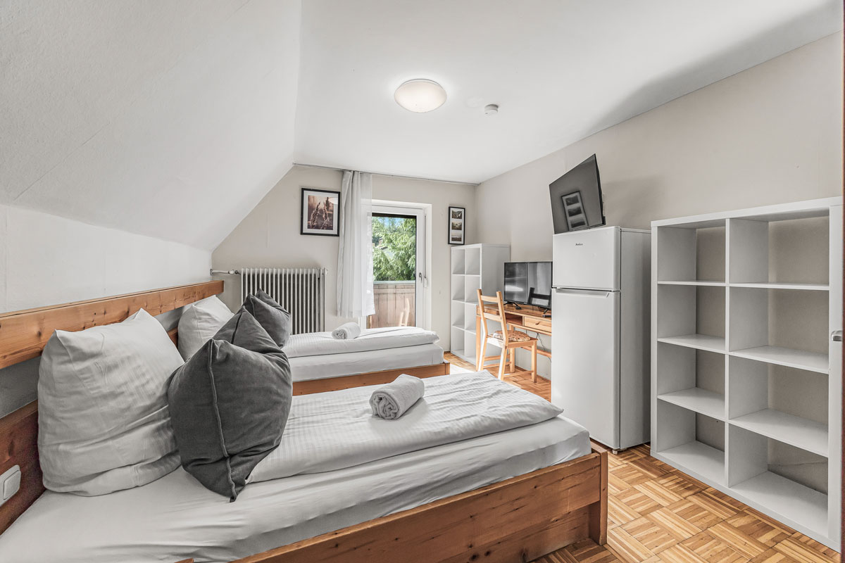 Helle, moderne Gästezimmer mit zwei Betten, Schreibtisch, Kühlschrank.