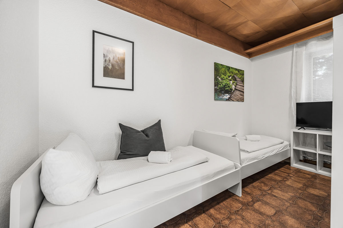 Zwei weiße Einzelbetten in minimalistischem Raum mit zwei Wandbildern.