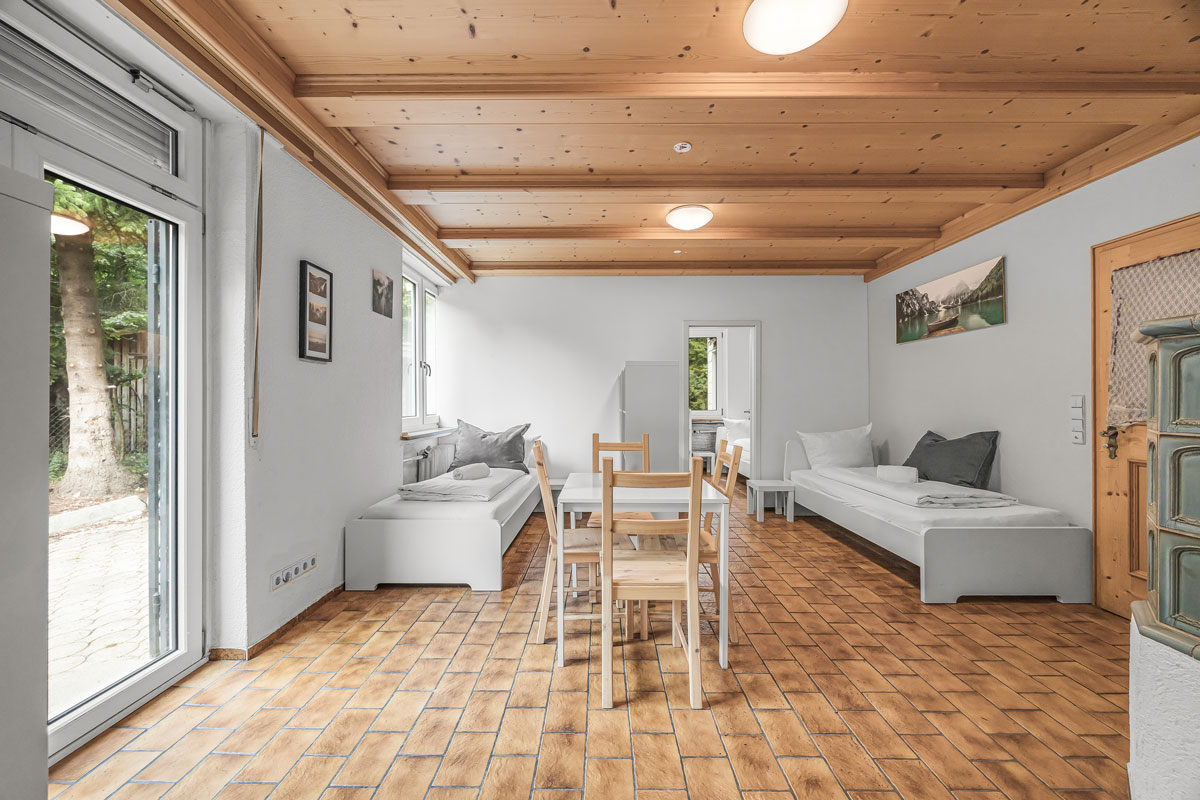 Heller Raum mit Holzboden und Decke, weiße Möbel und ein großes Fenster.