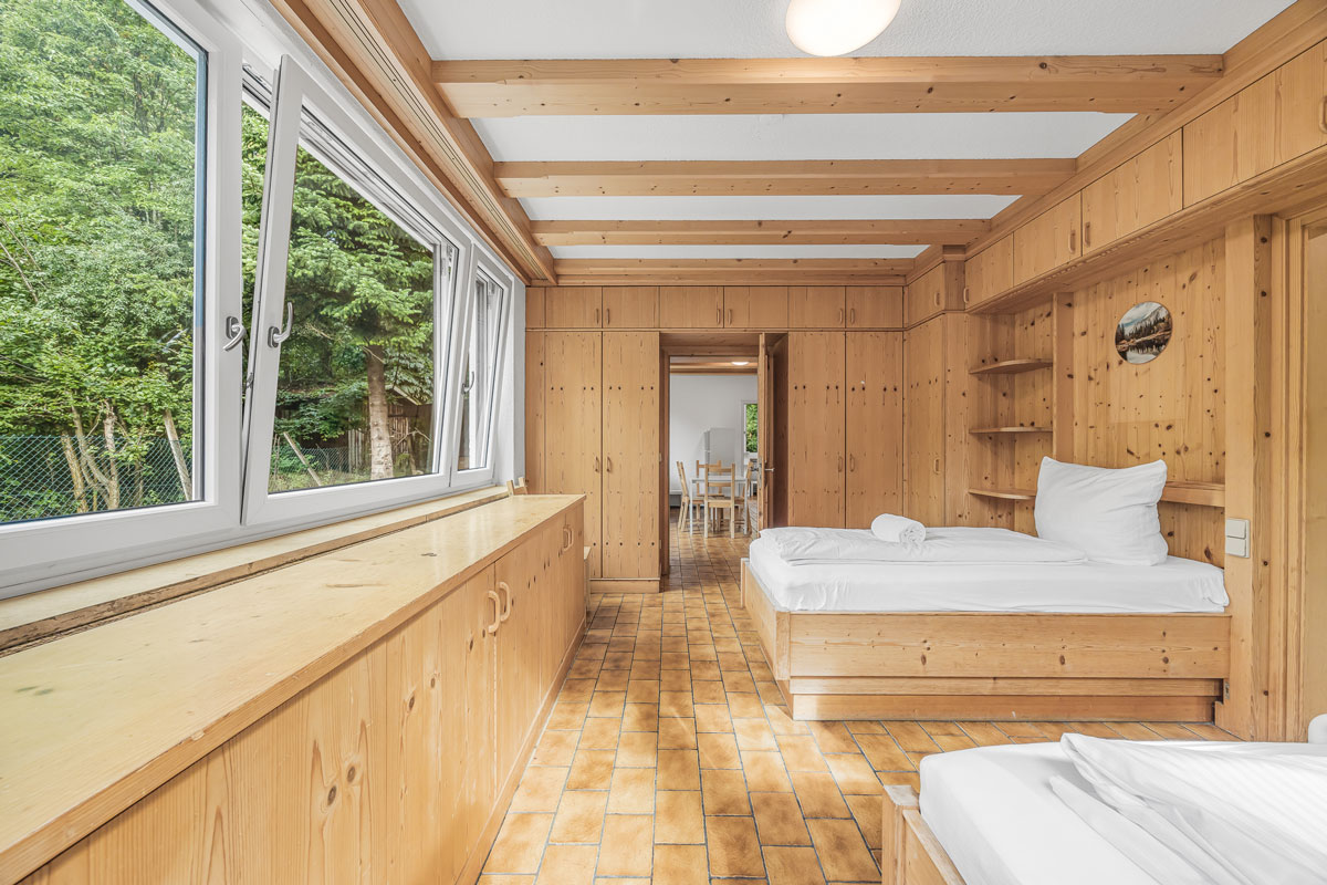 Helles Schlafzimmer mit holzverkleideten Wänden und großen Fenstern.