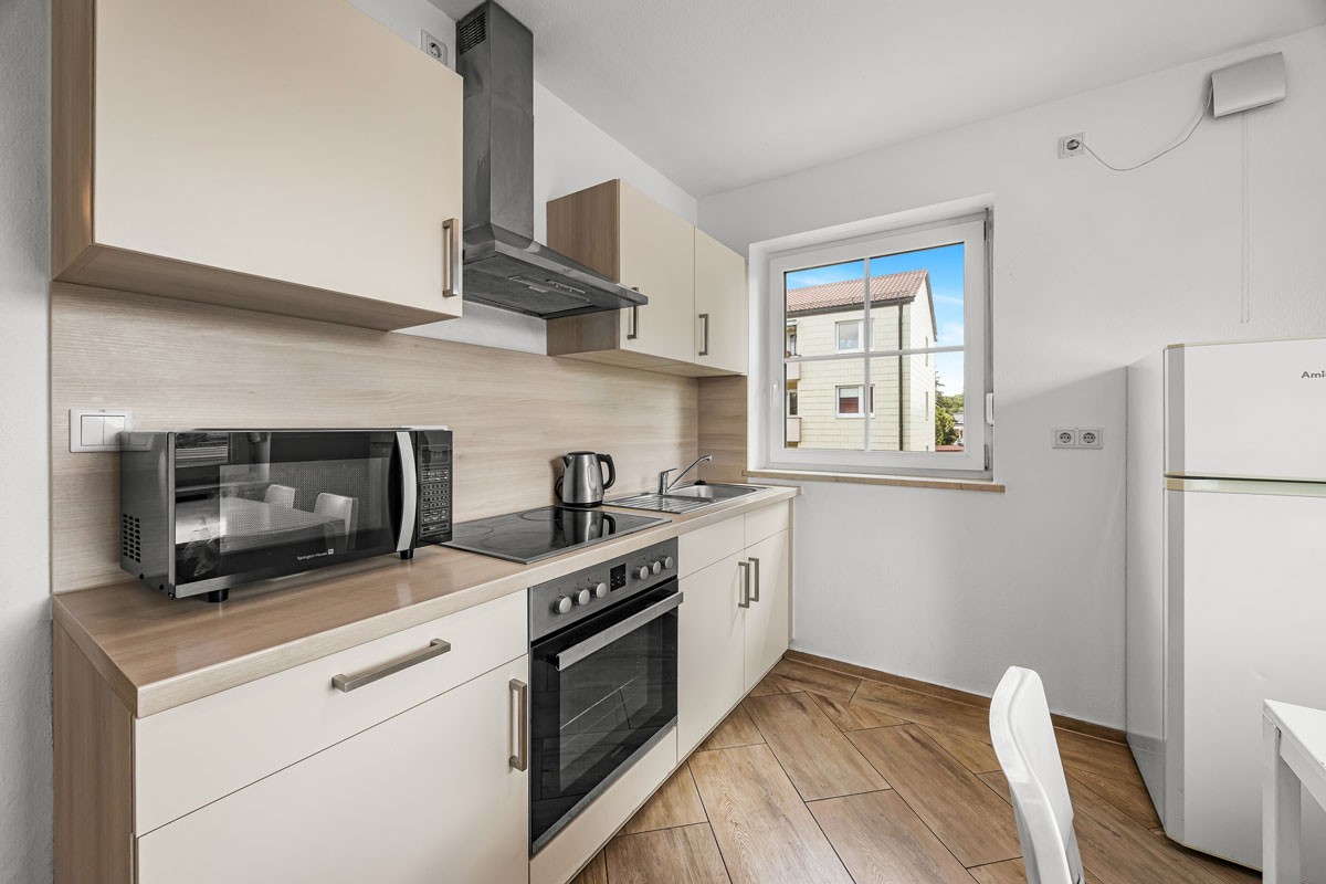 Moderne Küche, weiß, mit Geräten und Holzdetails, Fenster mit Tageslicht.