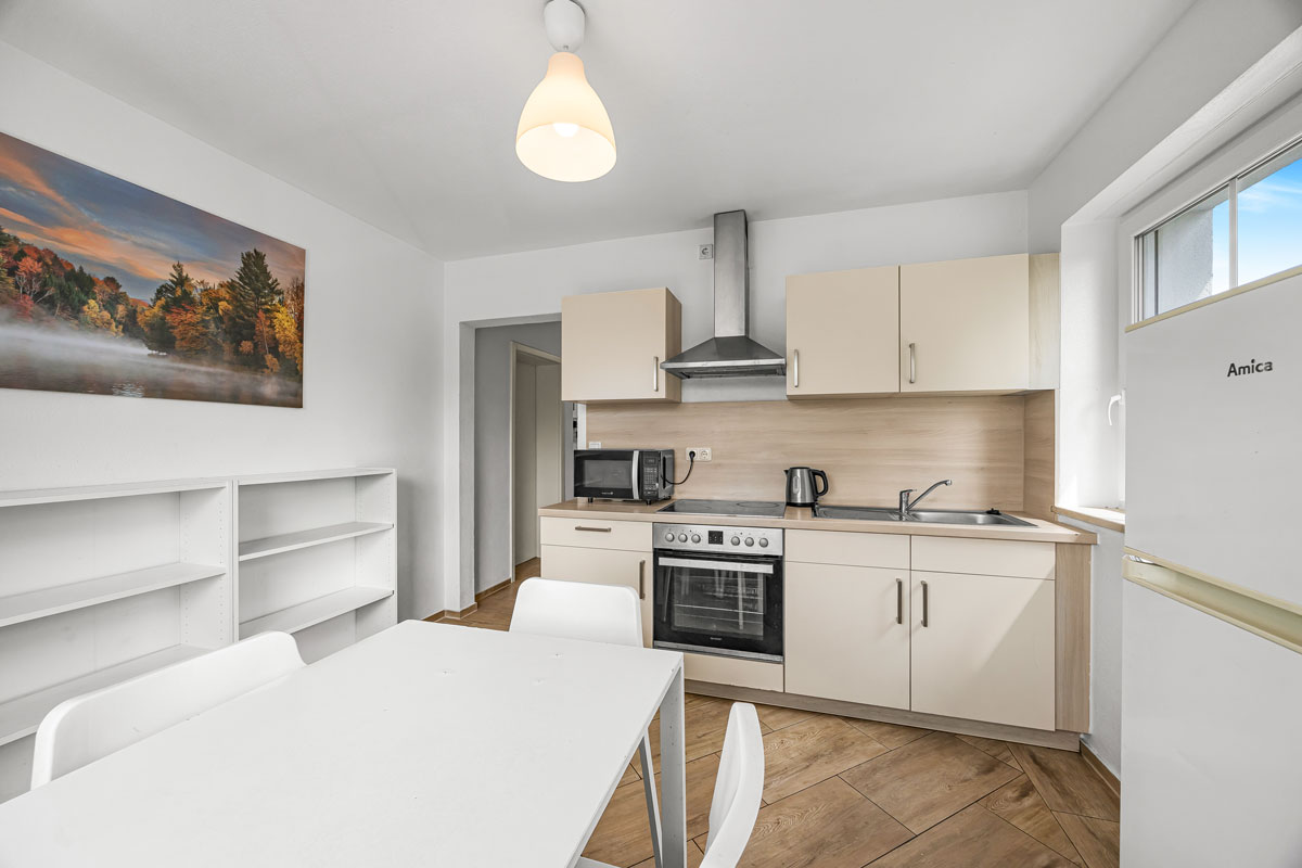 Helle Küche mit weißen Möbeln und einem farbenfrohen Landschaftsgemälde.