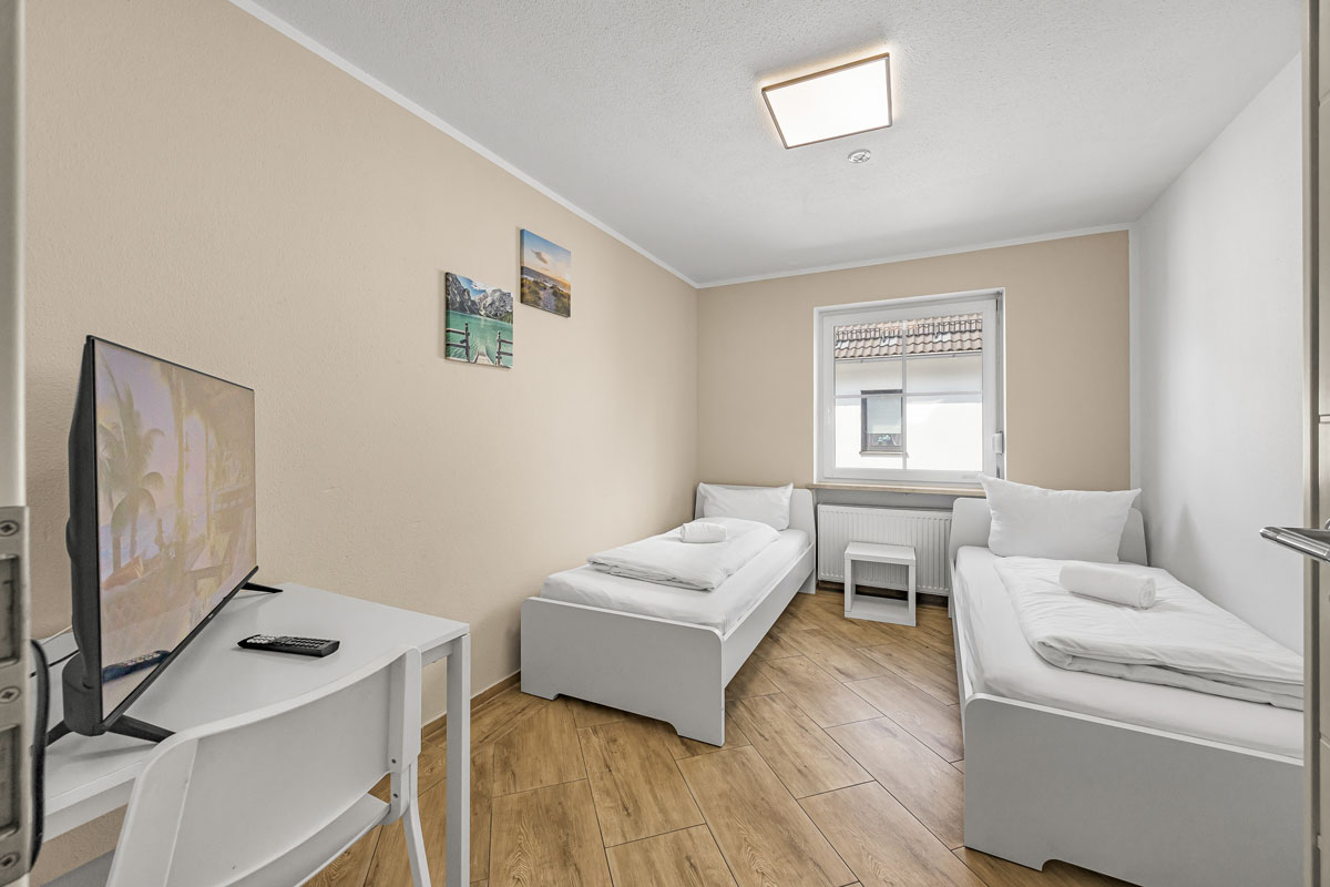 Ein helles Zimmer mit zwei Einzelbetten, Fernseher und Parkettboden.