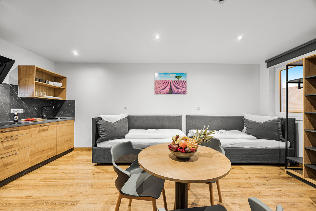 Moderne Küche mit Holzmöbeln, grauen Sofas, Tisch und Schüssel mit Obst.