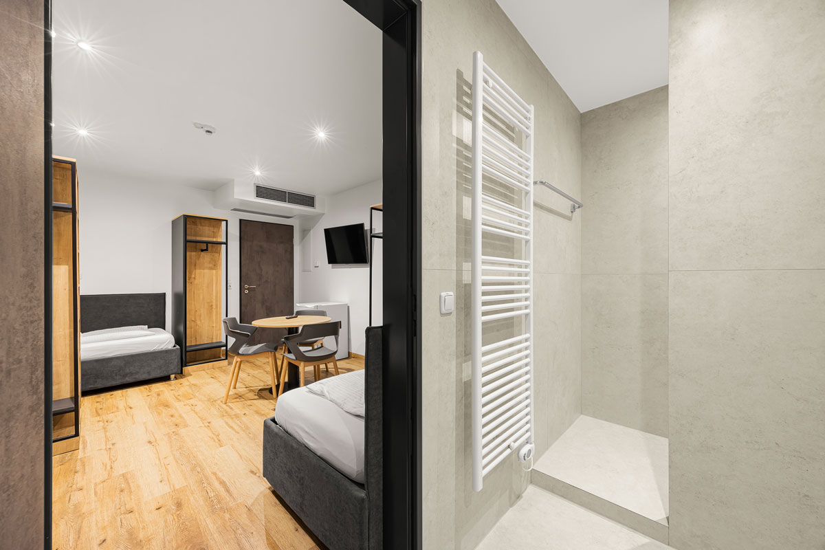 Modernes Hotelzimmer mit zwei Betten, Holzfußboden, Fernseher und Dusche.