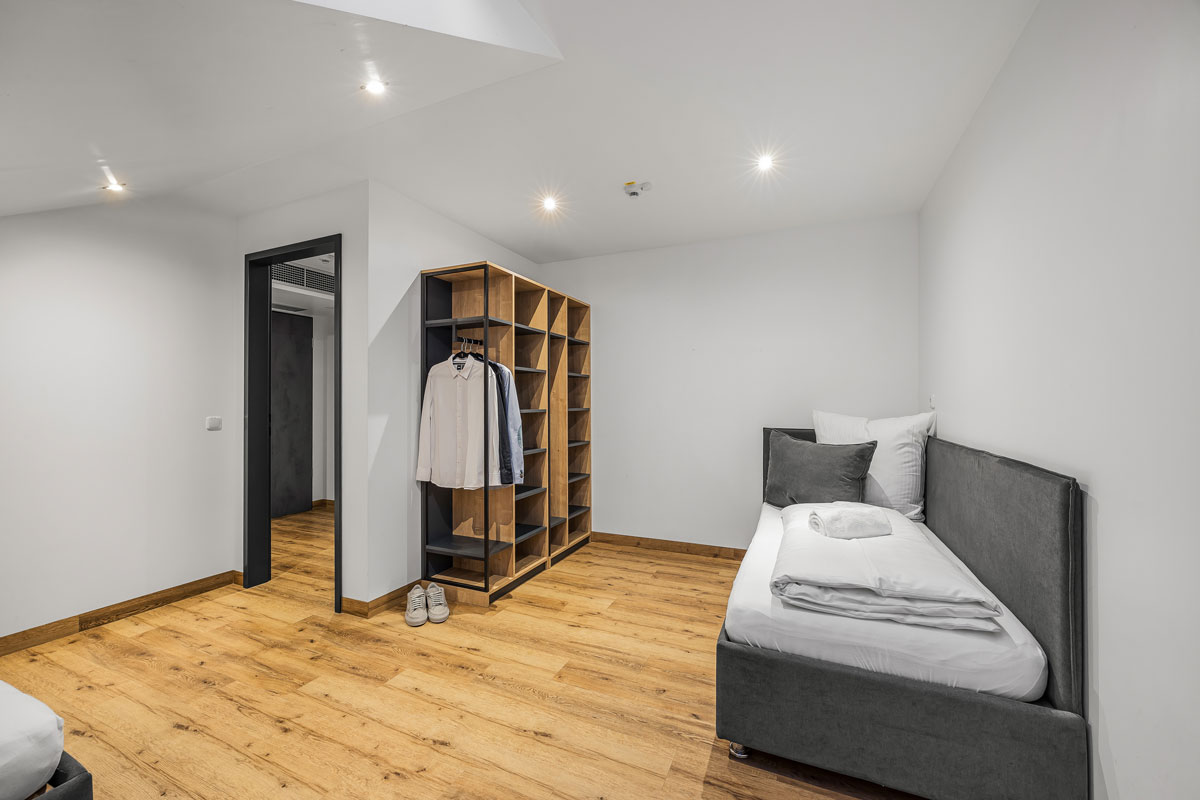 Minimalistisches Schlafzimmer mit Holzregal, grauem Bett und weißer Wand.