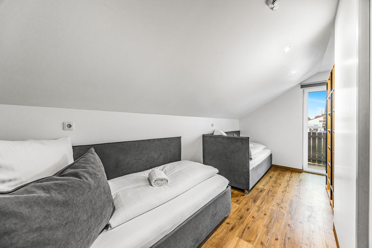 Ein Dachgeschosszimmer mit Holzboden, zwei grauen Betten und einem Fenster.