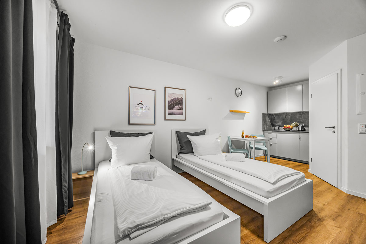 Helles Zimmer mit zwei Einzelbetten, heller Wand, schlichten Möbeln, Holzboden.