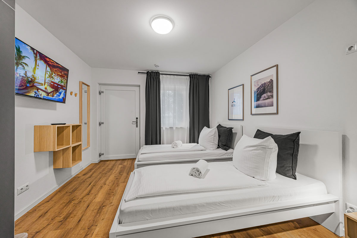 Modernes Zimmer mit zwei Einzelbetten, Holzboden und Kunst an der Wand.