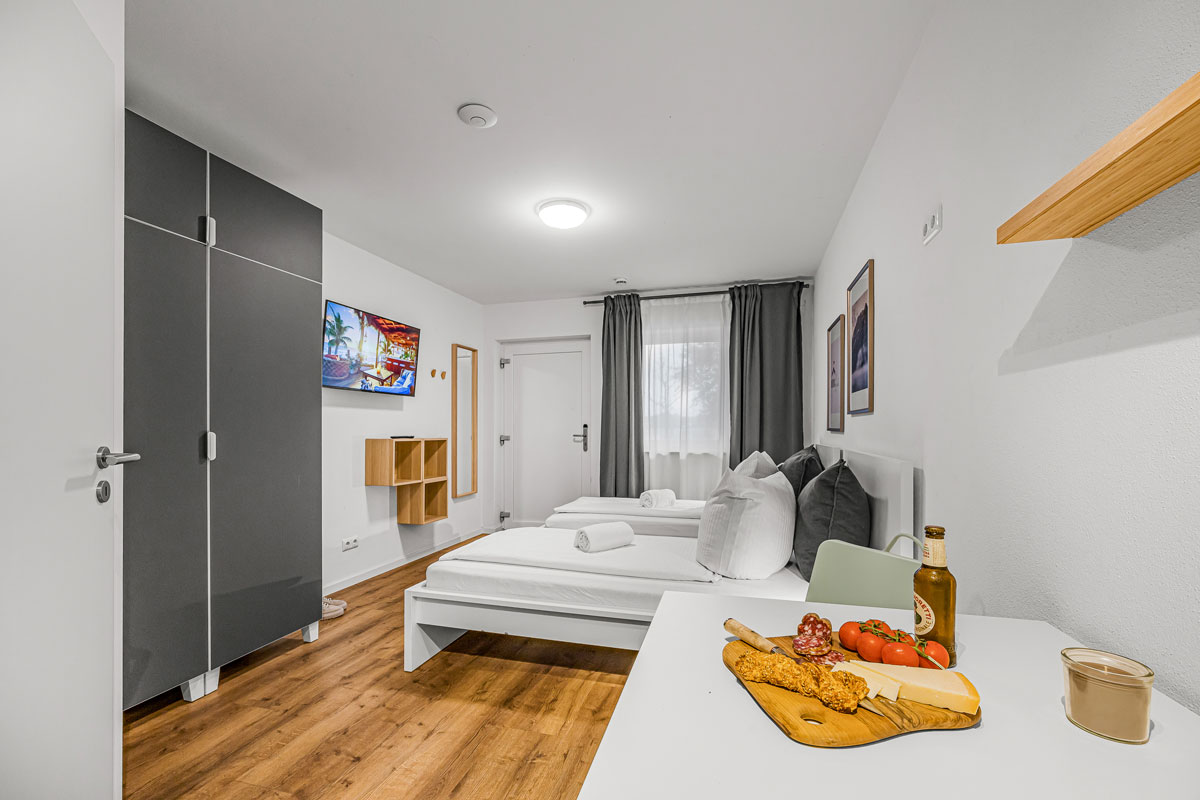 Modernes Zimmer mit Doppelbett, Holzboden, TV und minimalistischer Dekoration.