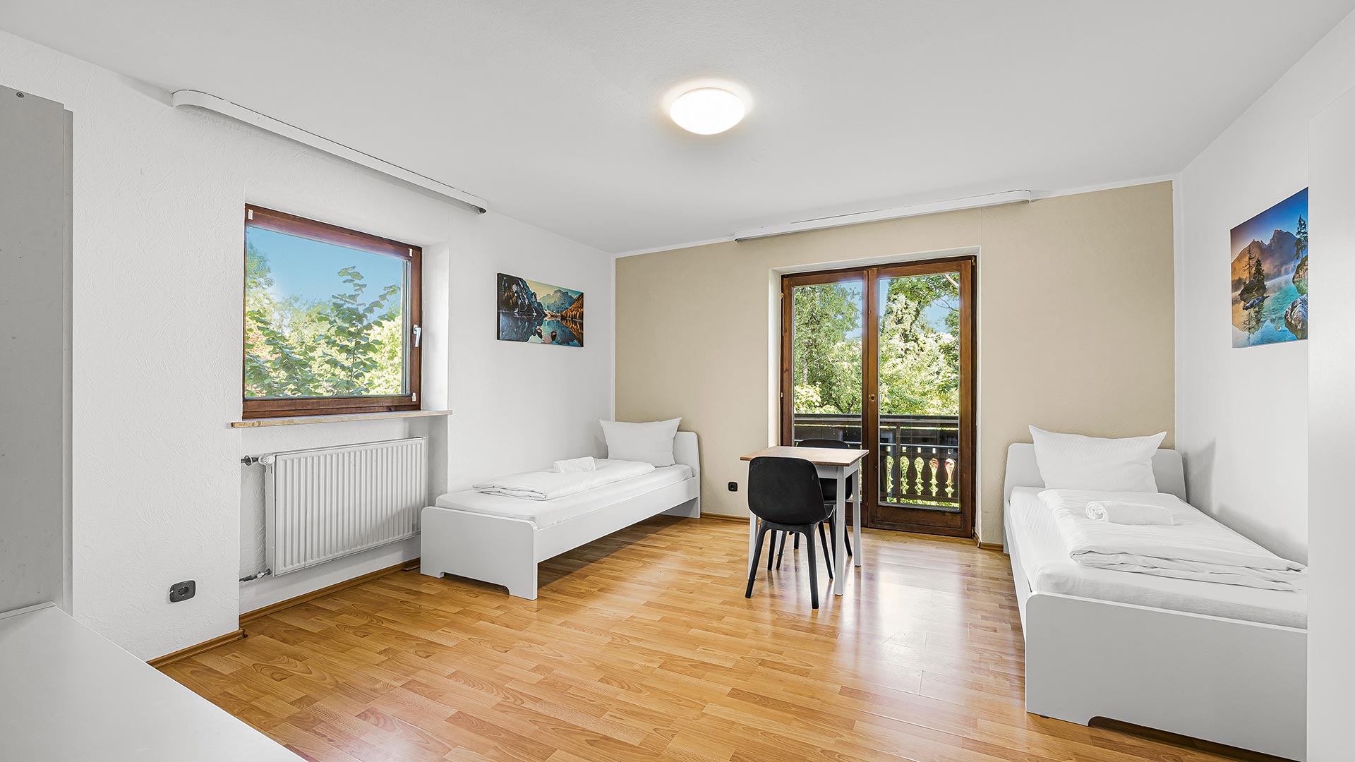 Ein helles Zimmer mit zwei Einzelbetten, Holzboden und großen Fenstern.