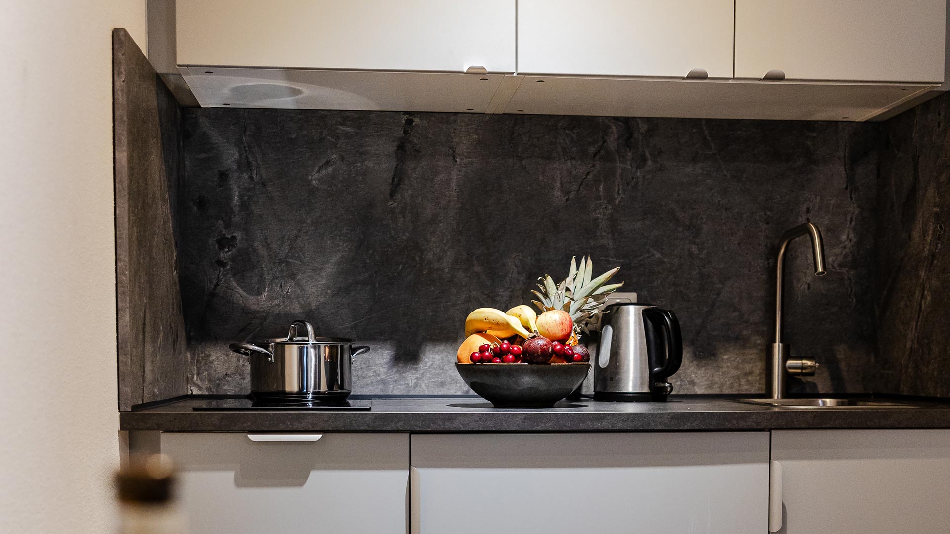 Eine moderne Küche mit einem Obstkorb voller bunter Früchte auf der Arbeitsplatte.