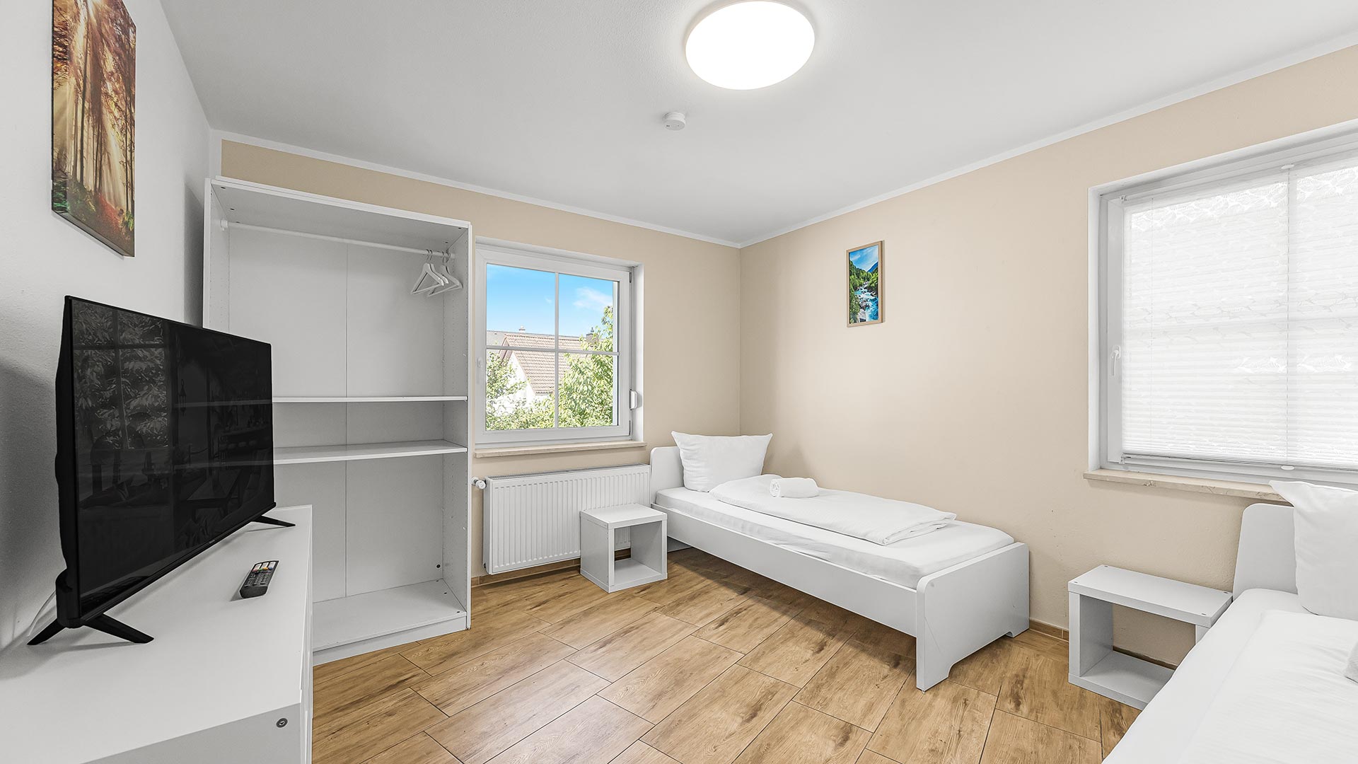 Ein helles Zimmer mit zwei Einzelbetten, einem weißen Kleiderschrank und einem Fernseher.