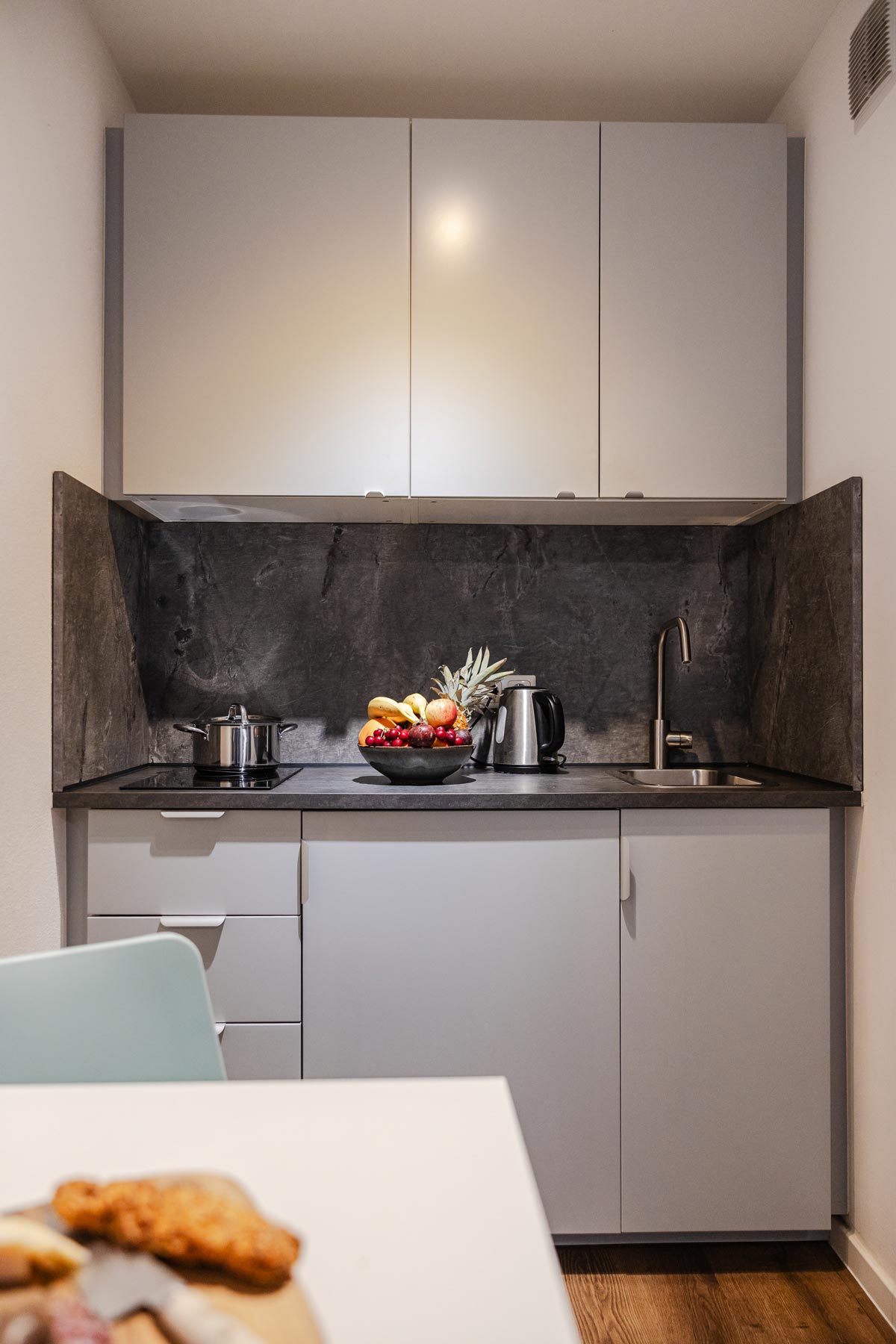 Moderne Küchenzeile mit grauen Schränken, dunkler Arbeitsplatte und frischem Obst.